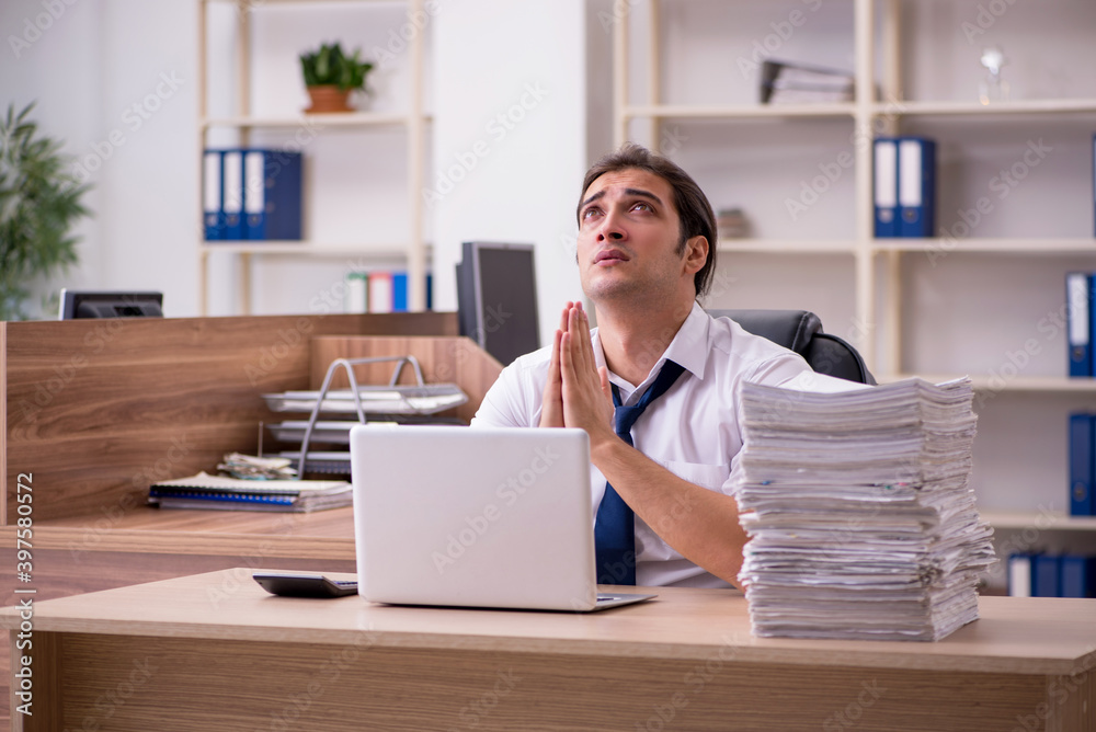 Young male employee unhappy with excessive work in the office Young male employee unhappy with excessive work in the office