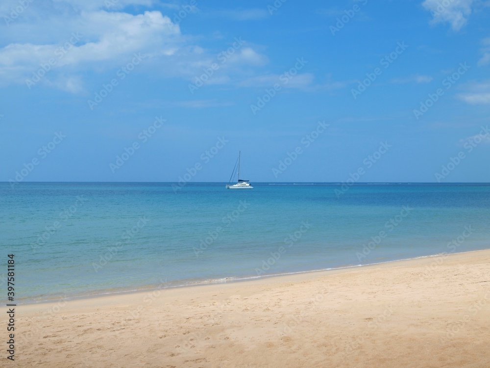 Seascape. Blue sea and sailing yacht on a horizon. White sand, empty beach. Sky with beautiful clouds. Lonely sailboat. Calm sea. Panorama of ocean. Sandy coast, clean shore. Panoramic view of resort.
