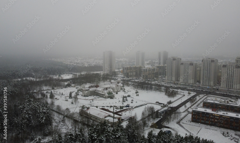 Top view of winter snowy city near forest on foggy evening