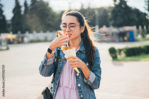 Asian girl eating street food French fries in paper bag
