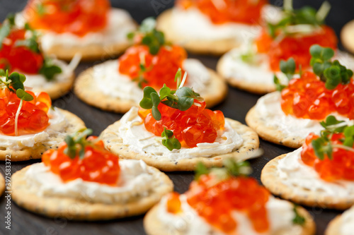 Salmon caviar and soft cheese savory crackers with sesame and poppy seeds served on black slate board