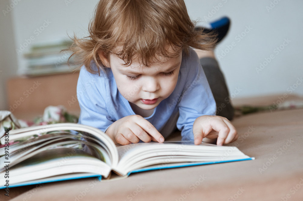 Cute preschooler boy reading a book with interest.