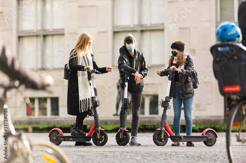 Trendy fashinable group of friends riding public rental electric scooters in urban city environment at fall. New eco-friendly modern public city transport in Ljubljana, Slovenia.