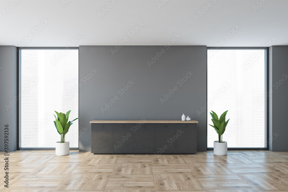 Grey office room with desk near wall, windows and plants in empty business room Grey office room with desk near wall, windows and plants in empty business room