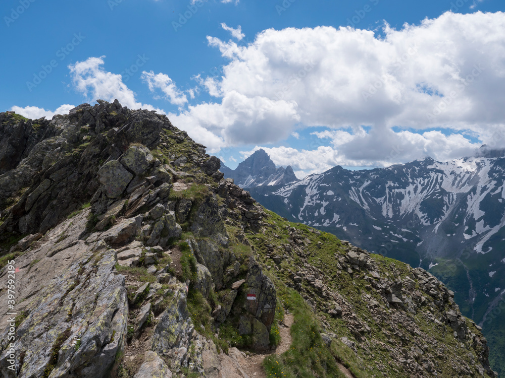 Snow-capped moutains and green valley on steep rocky footpath of Stubai hiking trail, Stubai Hohenweg, Alpine landscape of Tyrol Alps, Austria. Summer blue sky