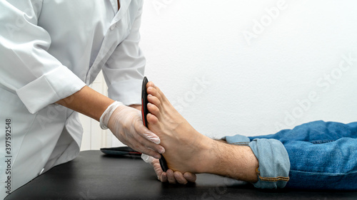 Close-up of a podiatrist trying out insoles on a patient. You can see the podiatrist s hands and the patient s foot on the table against a white background