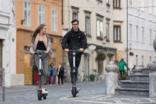 Trendy fashinable teenagers riding public rental electric scooters in urban city environment. New eco-friendly modern public city transport in Ljubljana, Slovenia.
