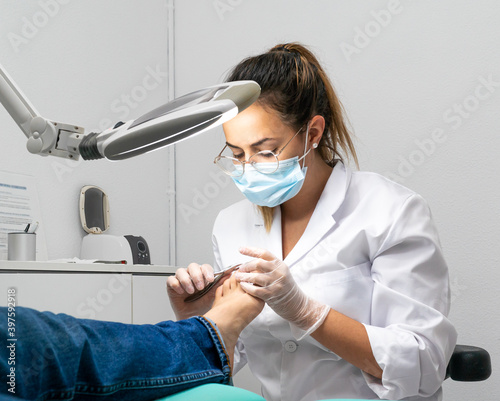Young podiatrist doing chiropody in her podiatry clinic. The chiropodist is cutting the patient's nails with specialized scissors photo