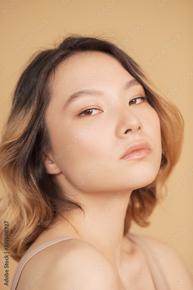 Concept beauty and fashion of face and body skin. Profile young girl of Asian appearance with wavy streaked hair on beige background Concept beauty and fashion of face and body skin. Profile young girl of Asian appearance with wavy streaked hair on beige background