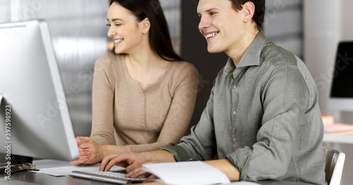 Smiling young businessmen and programmers are checking some data on computer, while sitting together in a modern office. Focus on man. Concept of successful business start up