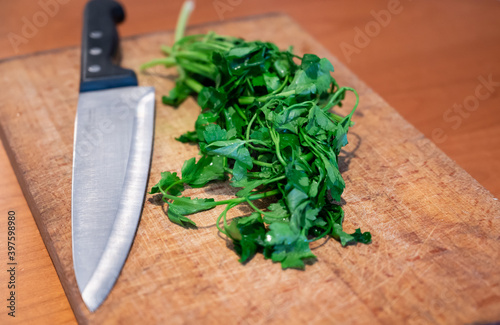Scenes of life at home: in the kitchen preparing chopped parsley on the cutting board. A large-blade knife and a bunch of fresh parsley rest on the cutting board.
