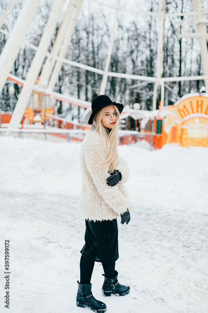 Stylish beautiful blonde girl in coat and hat posing in the park