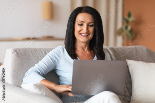 Mature woman sitting on sofa and working on computer