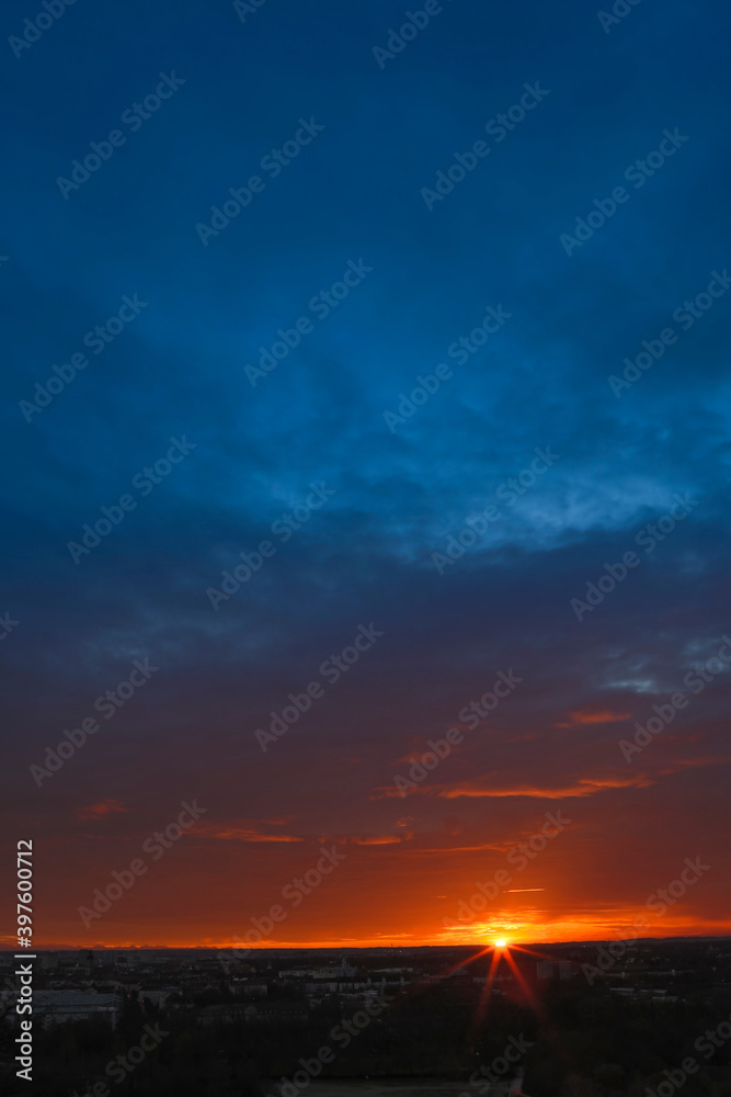 Dramatic sunset during autumn season with dark blue cloudy sky and bright orange and yellow horizon.