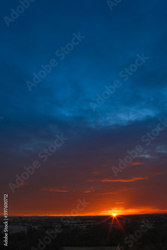 Dramatic sunset during autumn season with dark blue cloudy sky and bright orange and yellow horizon.