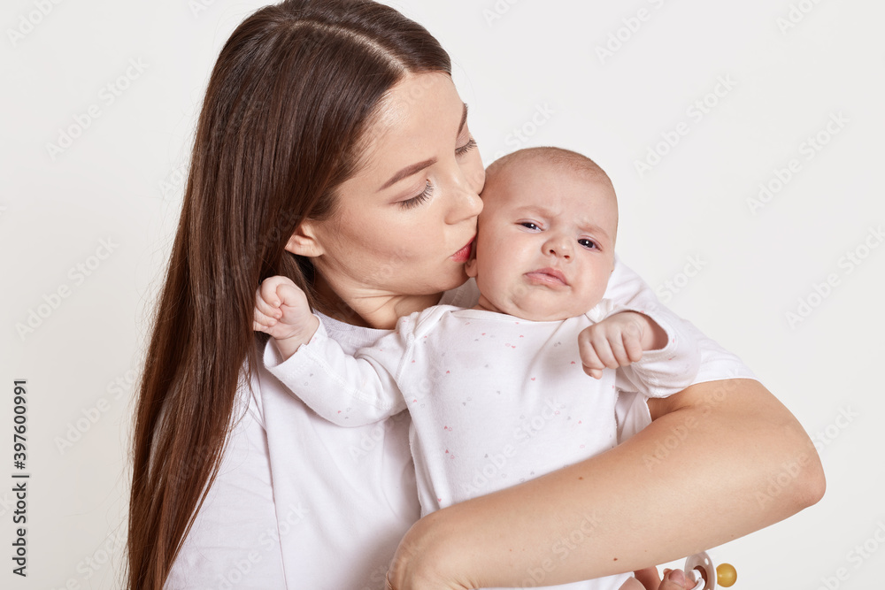 Mother kissing and hugging newborn daughter isolated over white background, tender, care, lady with brown hair expressing love to her child. Mother kissing and hugging newborn daughter isolated over white background, tender, care, lady with brown hair expressing love to her child.