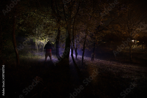 strange light in a dark forest at night. Silhouette of person standing in the dark forest with light. Horror halloween concept. strange silhouette in a dark spooky forest at night