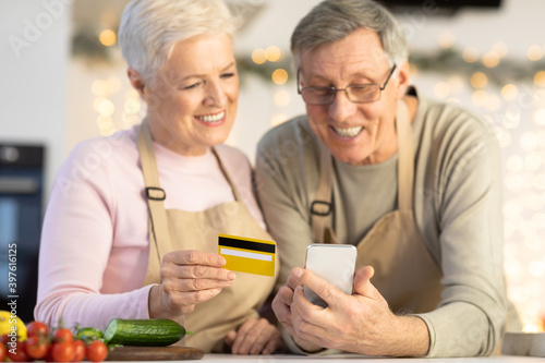 Senior Spouses Shopping With Smartphone And Credit Card In Kitchen