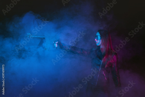 Futuristic girl soldier with a gun in the smoke on the dark background. © Dmitriy
