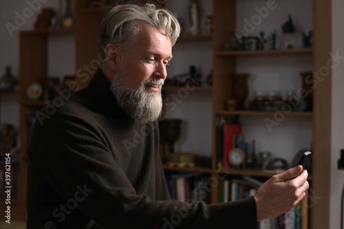 An adult gray-haired man with a beard makes a video call to his relatives, side view