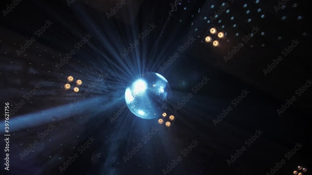 Mirror disco ball spinning and reflecting blue rays of light in a ...