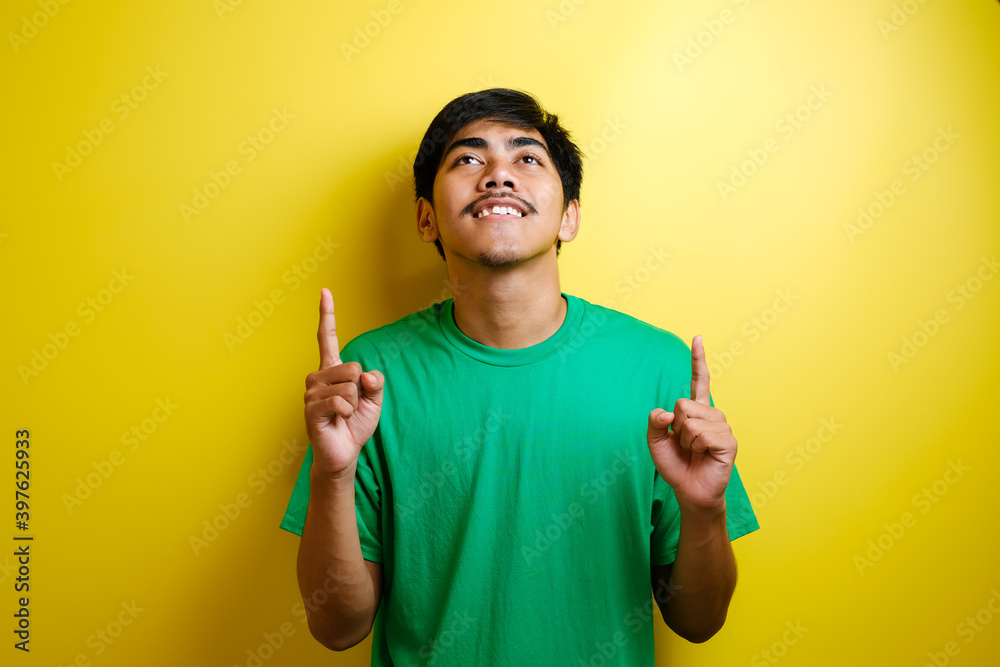 Asian young man in green t-shirt looked happy thinking and looking up, having good idea Asian young man in green t-shirt looked happy thinking and looking up, having good idea