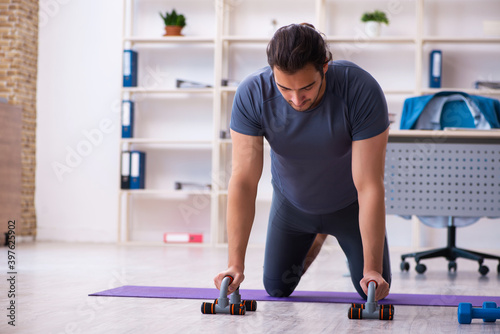 Young handsome employee doing sport exercises in the office