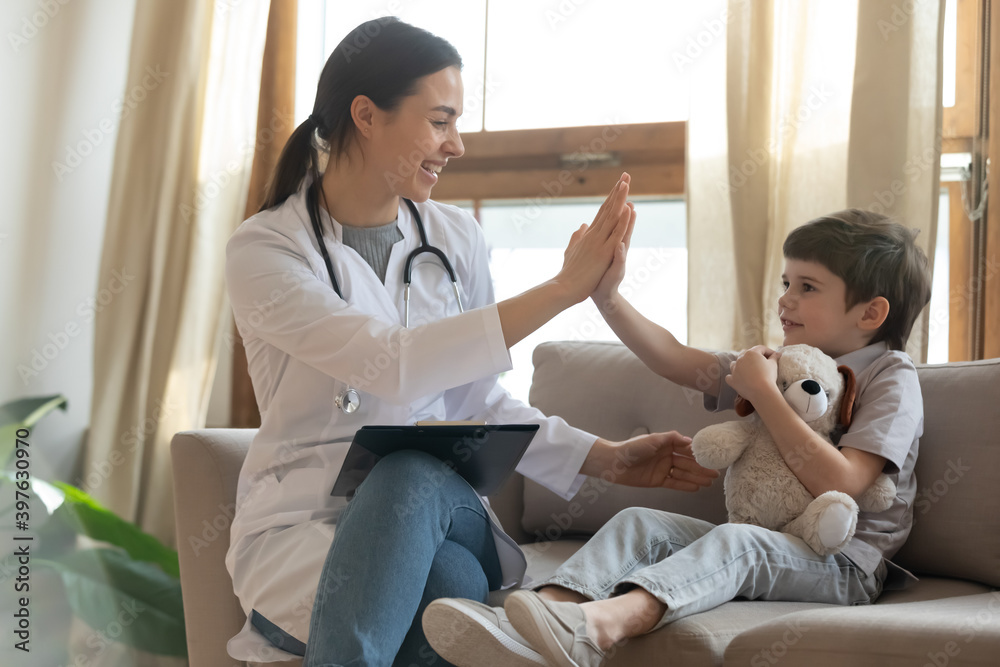 Obraz premium Smiling young female doctor give high five to caucasian little boy patient at consultation in clinic. Happy caring woman pediatrician greet with small child at checkup in hospital. Healthcare concept
