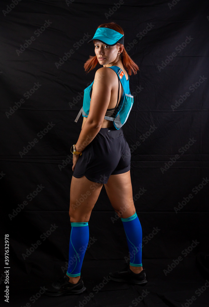 Beautiful redhead girl in jogging uniform posing in studio on black background