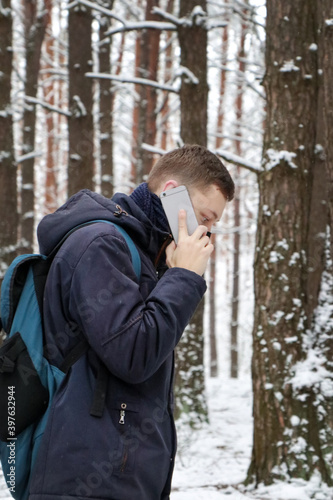 A man in a blue jacket and mask is talking on the phone. Winter forest walk. Modern gray gadget in human hands.