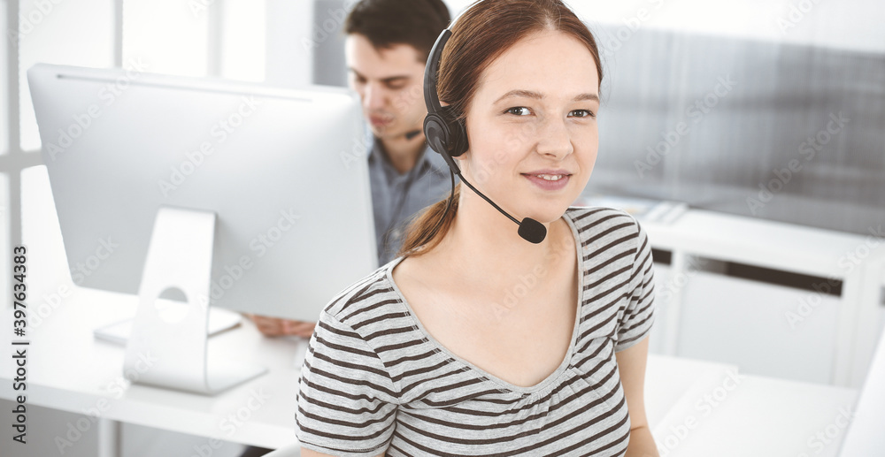 Casual dressed young woman using headset and computer while talking with customers online. Group of operators at work. Call center, business concept Casual dressed young woman using headset and computer while talking with customers online. Group of operators at work. Call center, business concept