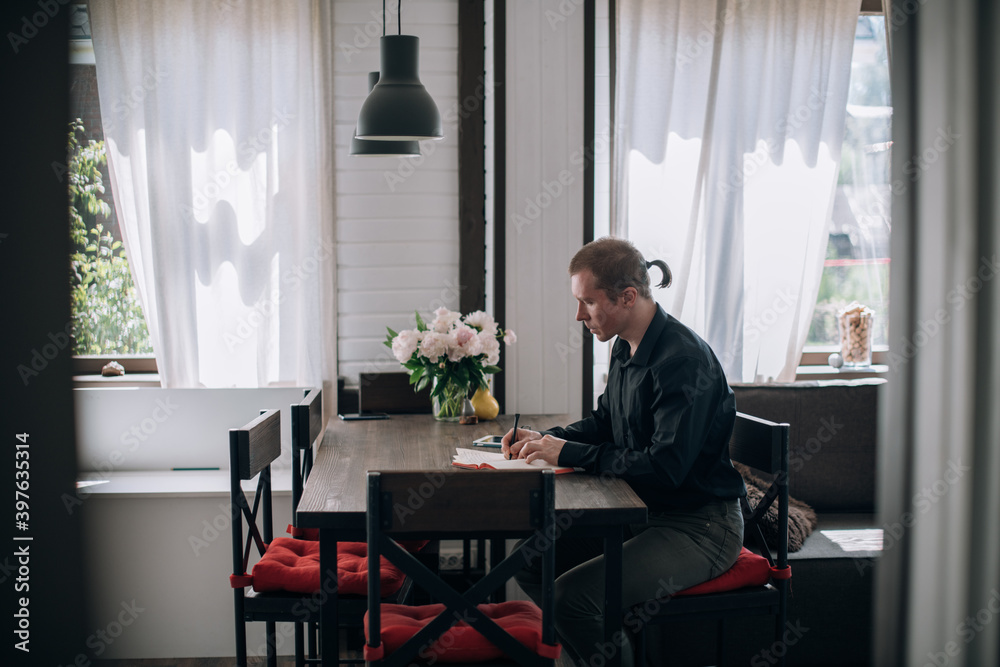 A young man writes in a notebook at the table A young man writes in a notebook at the table