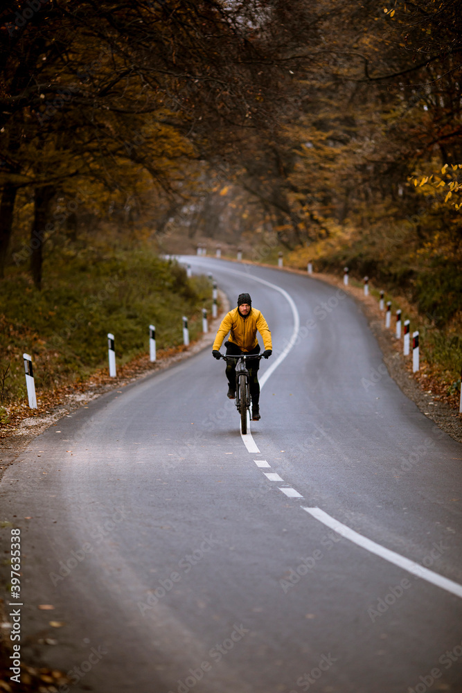 Young man biking on a country road through autumn forest