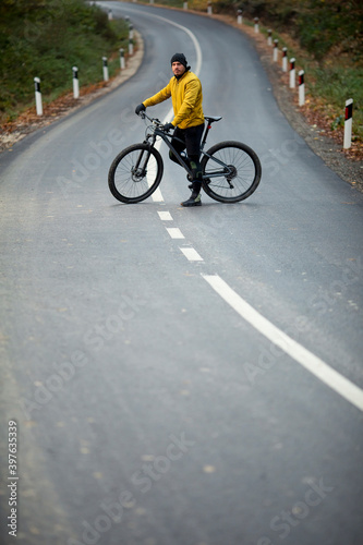 Young man taking a brake on a country road during biking through autumn forest