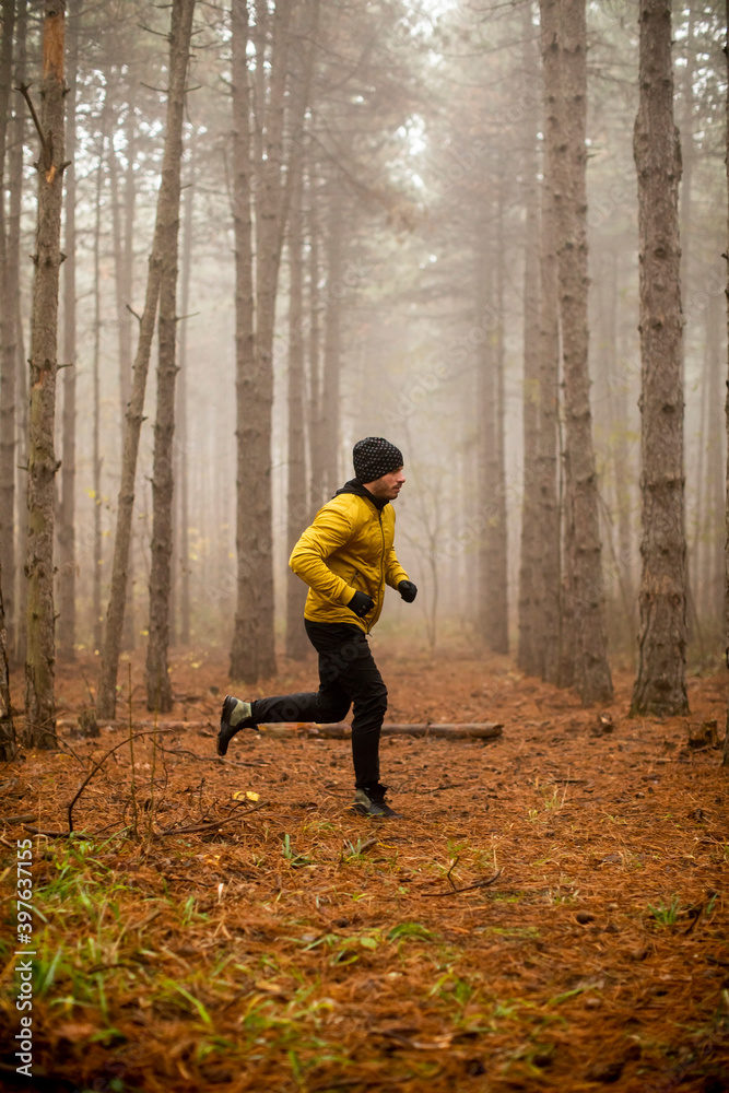 Young man running in autumn forest and exercising for trail run marathon endurance race