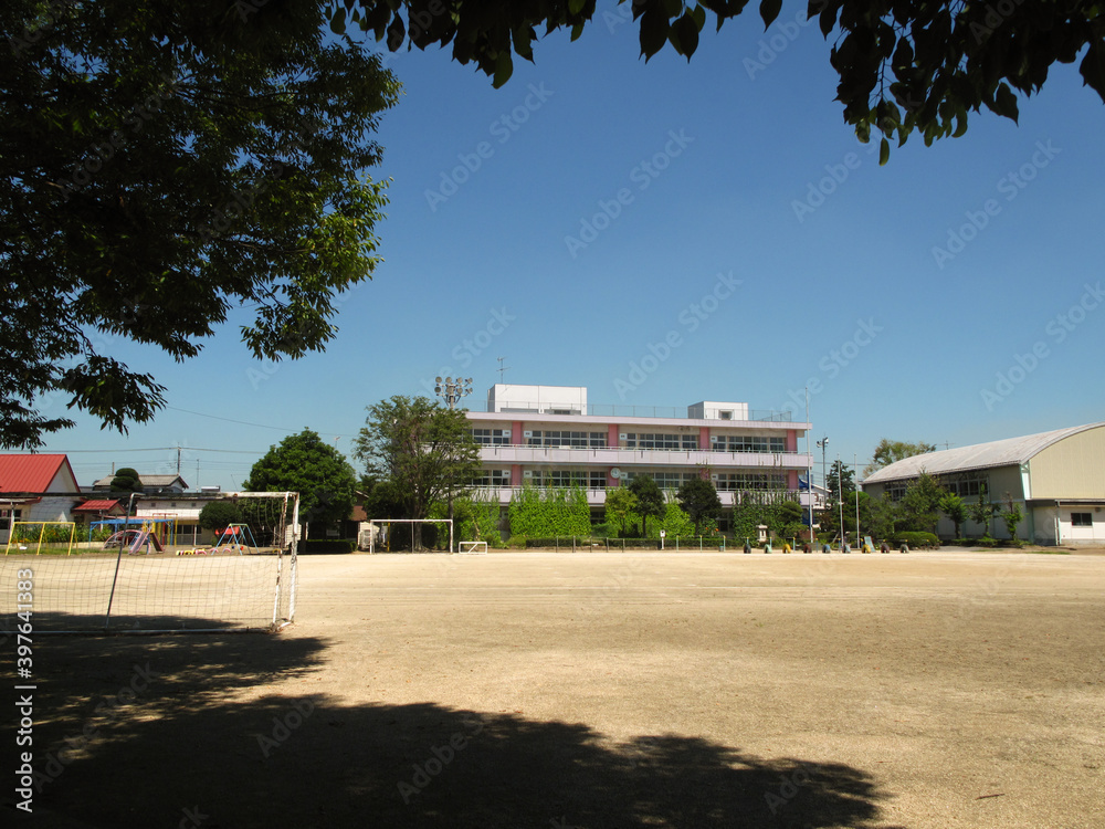 A wide view of a traditional multi-level Japanese school with exercise equipment and an empty yard in the foreground on a sunny day A wide view of a traditional multi-level Japanese school with exercise equipment and an empty yard in the foreground on a sunny day