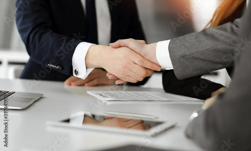 Unknown businessman shaking hands with his colleague or partner above the desk in sunny office, close-up
