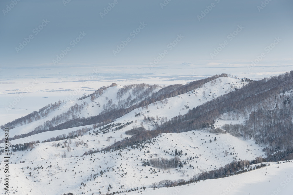 Gentle slopes of forest hills are covered with first snow. View of mountain valleys and ridge on horizon. Gentle slopes of forest hills are covered with first snow. View of mountain valleys and ridge on horizon.