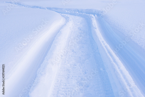 Snowmobile tracks in deep snow. Twisting traces of a snowmobile crossing snow covered field © Koirill