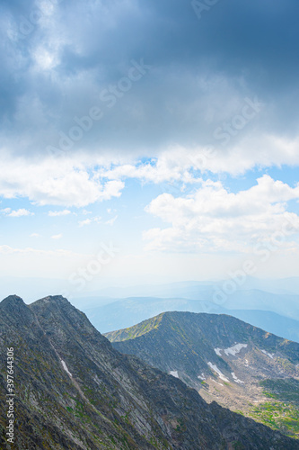Panoramic view of rocky ridge. Mountains on horizon under cloudy sky. Travel through mountain valley on sunny day.