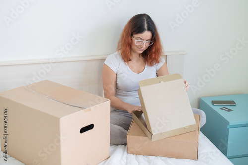Caucasian woman opens an order while sitting in bed. Online shopping concept with home delivery