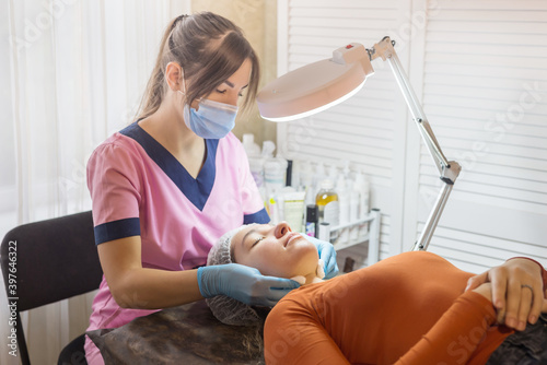 Cosmetologist cleaning face of a young woman with a cotton pads.