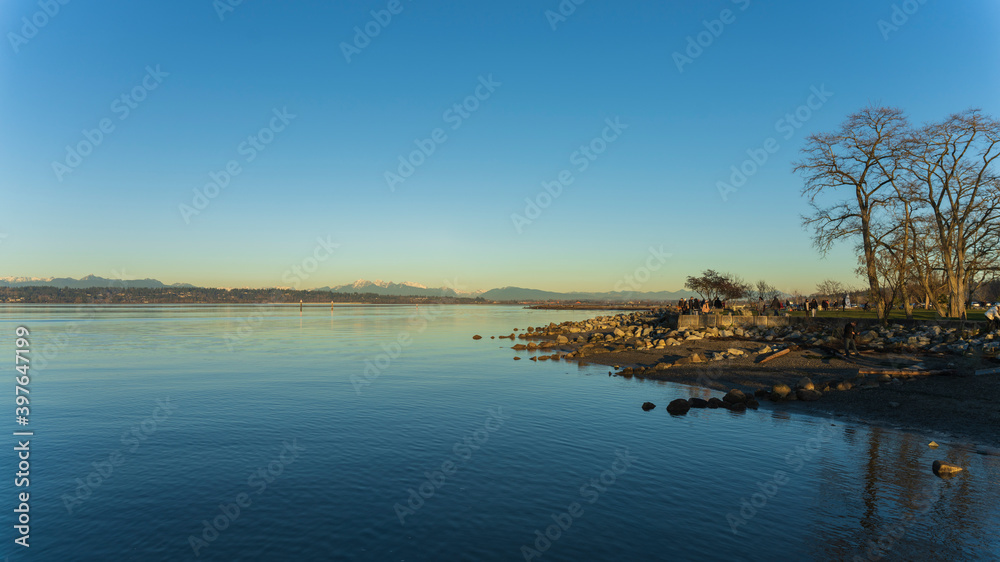 Public park and walking trail at natural BC beach by bay in early winter with snow-capped mountains on horizon Public park and walking trail at natural BC beach by bay in early winter with snow-capped mountains on horizon