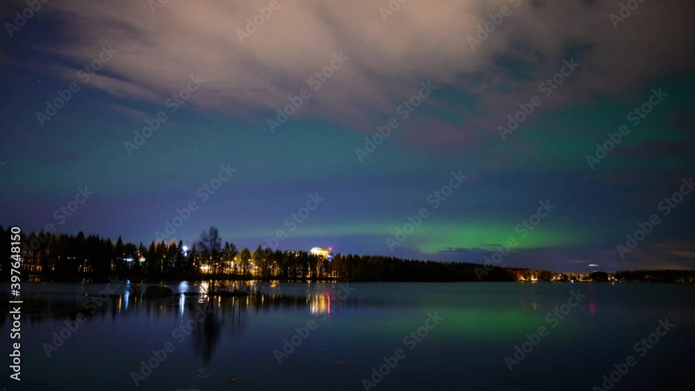 A 4k HD time-lapse of northern light dancing over a half-frozen lake and cloudy city light with reflection from the water A 4k HD time-lapse of northern light dancing over a half-frozen lake and cloudy city light with reflection from the water