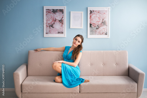 beautiful pregnant woman in a blue dress is sitting on the sofa.