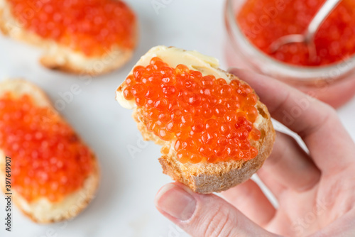 Red caviar and butter on slice of baguette bread in female hand. Tasty healthy luxury appetizer canape