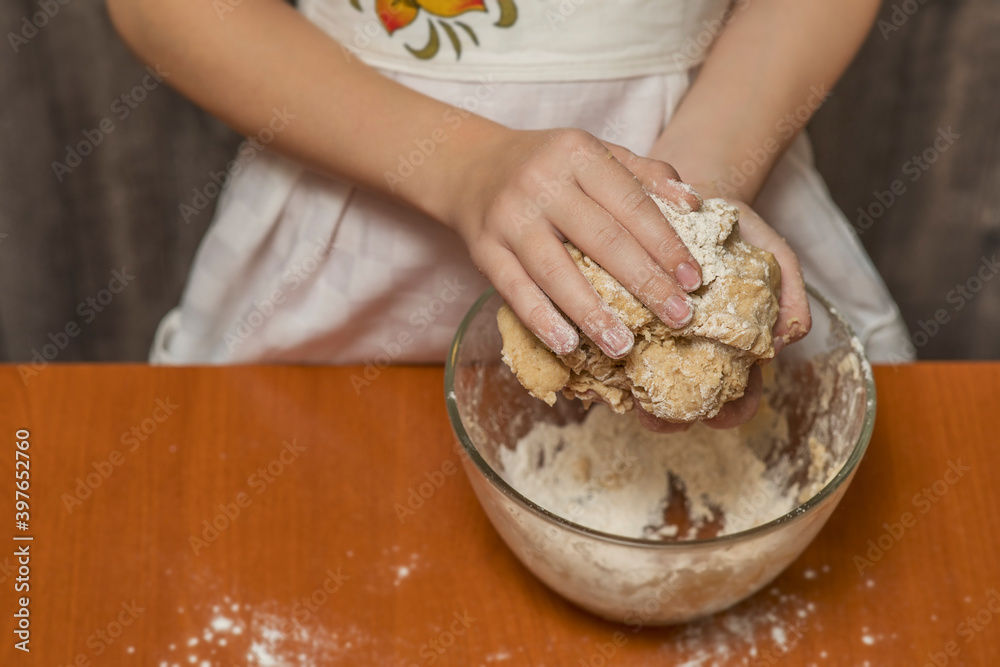 A girl in a kitchen apron is kneading cookie dough. Homemade baking.
