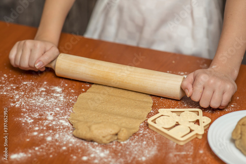 The little chef rolls out the cookie dough with a rolling pin on the table. Homemade cakes on the eve of Christmas.