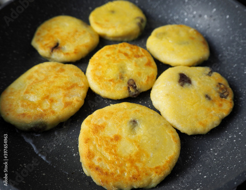 seven yellow curd cheesecakes without sugar with a banana in corn flour fried in coconut oil in a gray frying pan side view . cooking cheesecakes at home