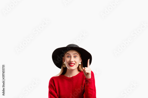 Trend offer. Fashion look. Information banner. Sales discount. Happy inspired woman in stylish sweater and wide-brimmed hat pointing up copy space isolated on white. Advertising background.